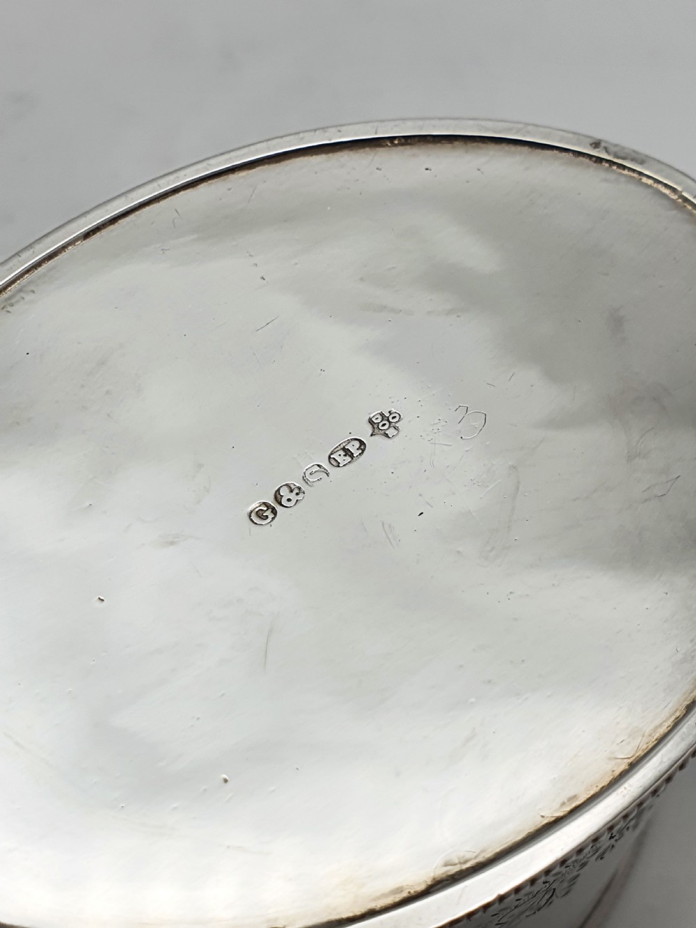 An oval silver-plated tea caddy featuring engraved foliate garlands on the body and lid, accompanied by a small shell-shaped spoon. View VIII
