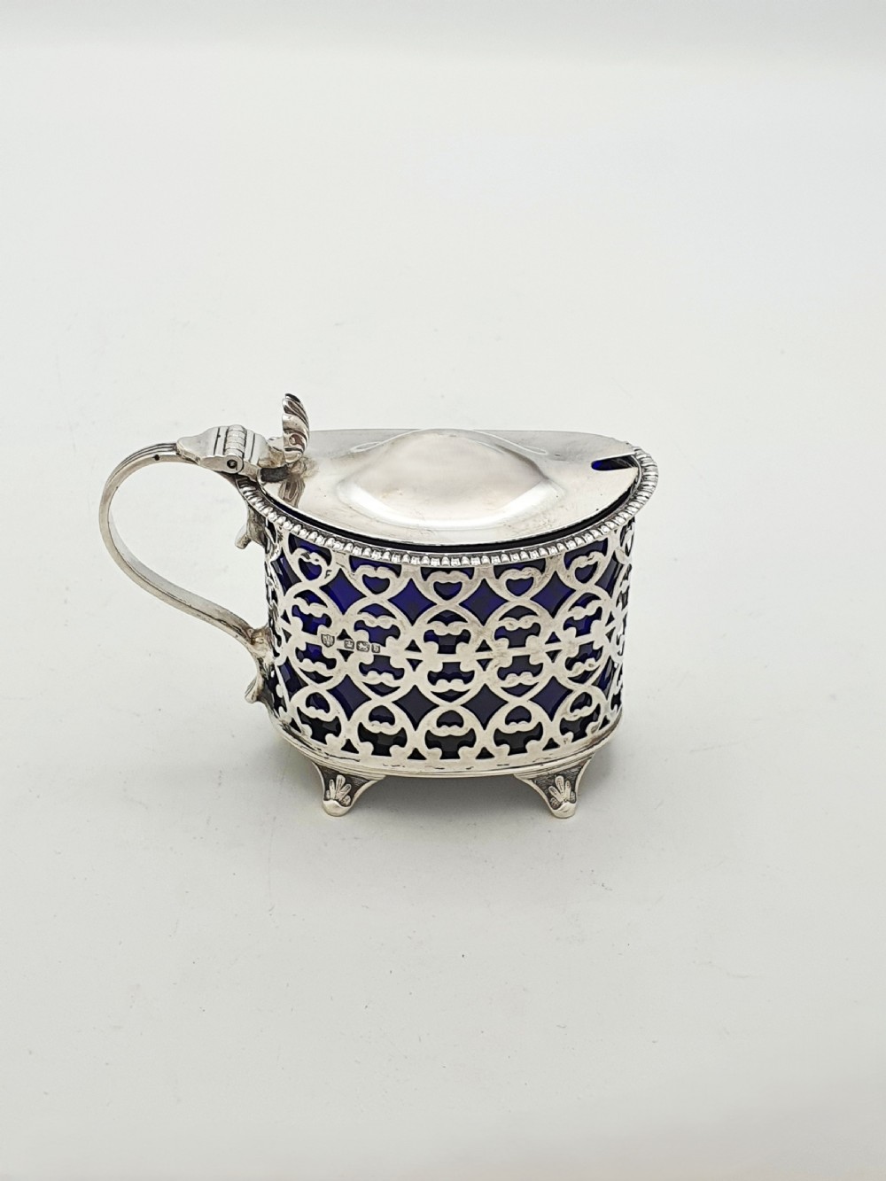 A Victorian sterling silver mustard pot with openwork lattice piercing, a hinged lid, a scroll handle, and a removable cobalt blue glass liner.