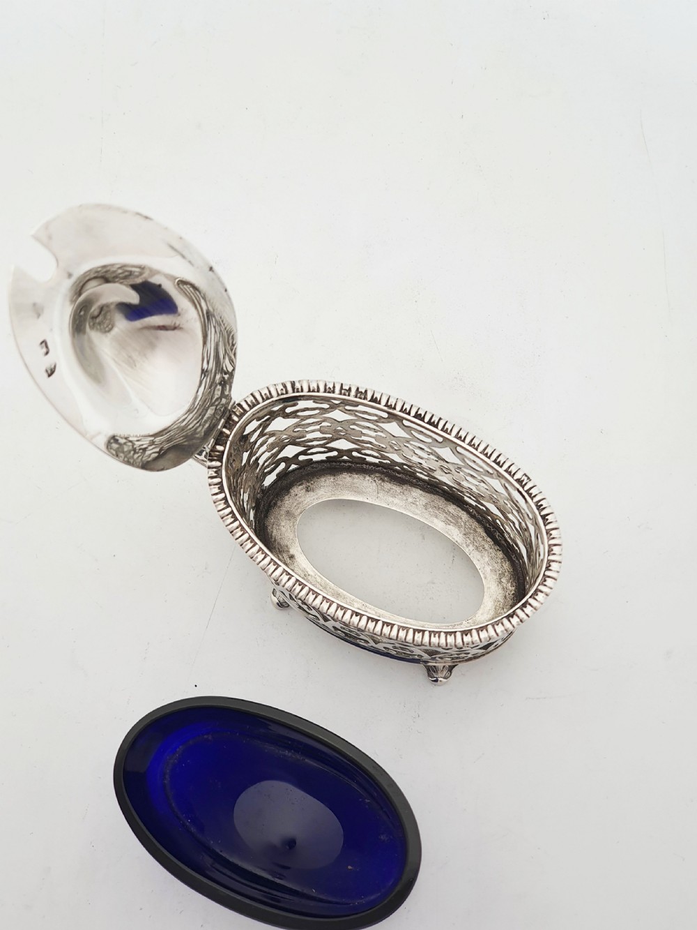 A Victorian sterling silver mustard pot with openwork lattice piercing, a hinged lid, a scroll handle, and a removable cobalt blue glass liner. View V