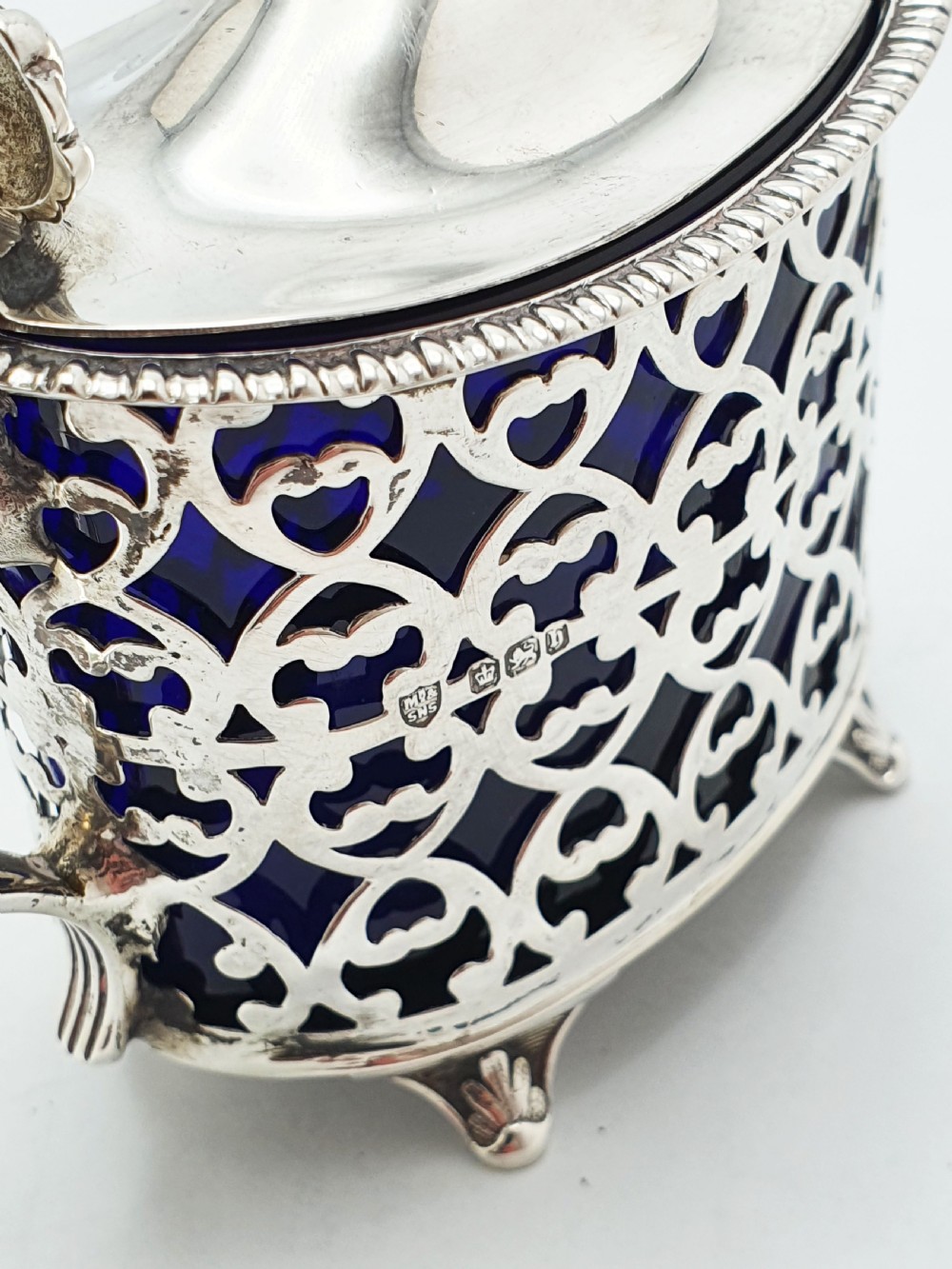 A Victorian sterling silver mustard pot with openwork lattice piercing, a hinged lid, a scroll handle, and a removable cobalt blue glass liner. View VII