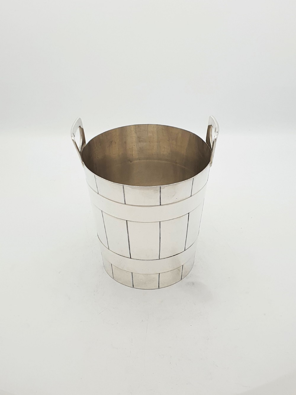 An Edwardian silver-plated ice bucket shaped like a wooden barrel with integrated handles alongside matching claw-foot ice tongs. View IV