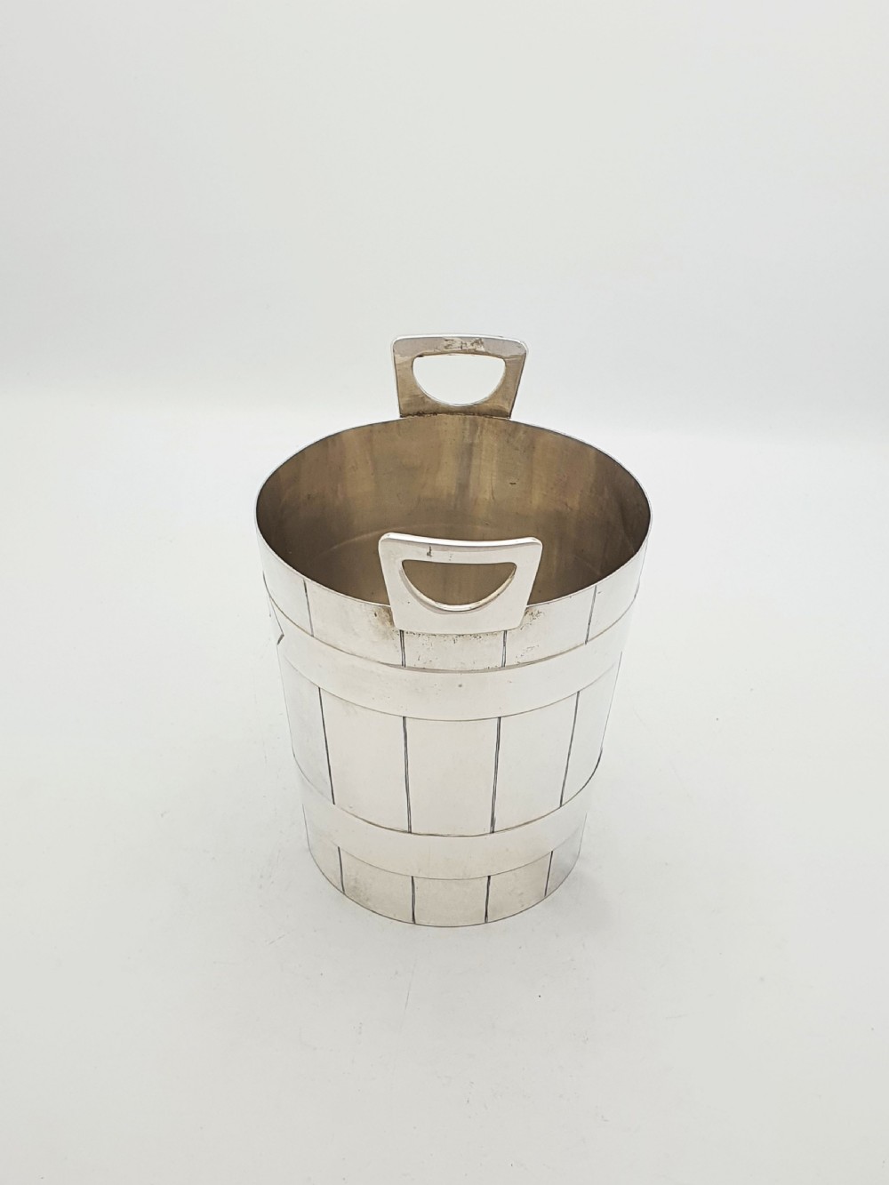 An Edwardian silver-plated ice bucket shaped like a wooden barrel with integrated handles alongside matching claw-foot ice tongs. View V