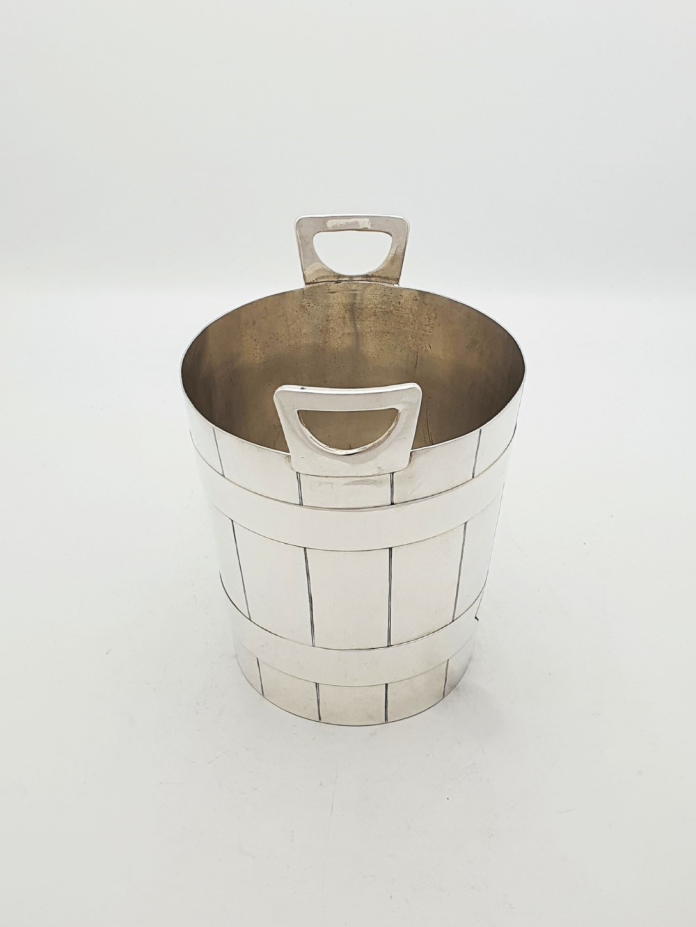 An Edwardian silver-plated ice bucket shaped like a wooden barrel with integrated handles alongside matching claw-foot ice tongs. View VI