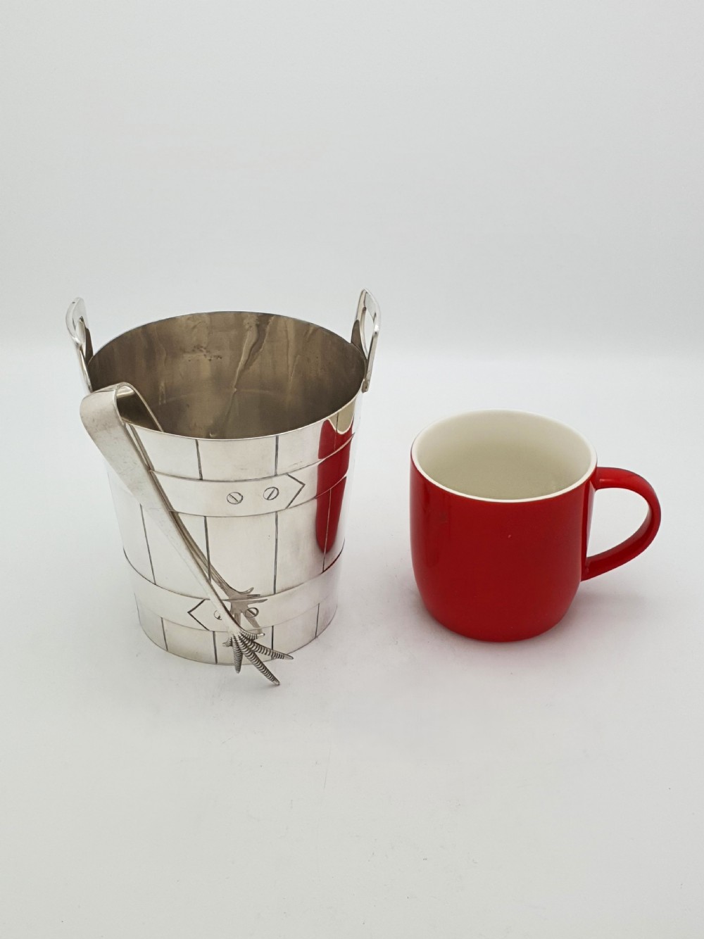 An Edwardian silver-plated ice bucket shaped like a wooden barrel with integrated handles alongside matching claw-foot ice tongs. View X