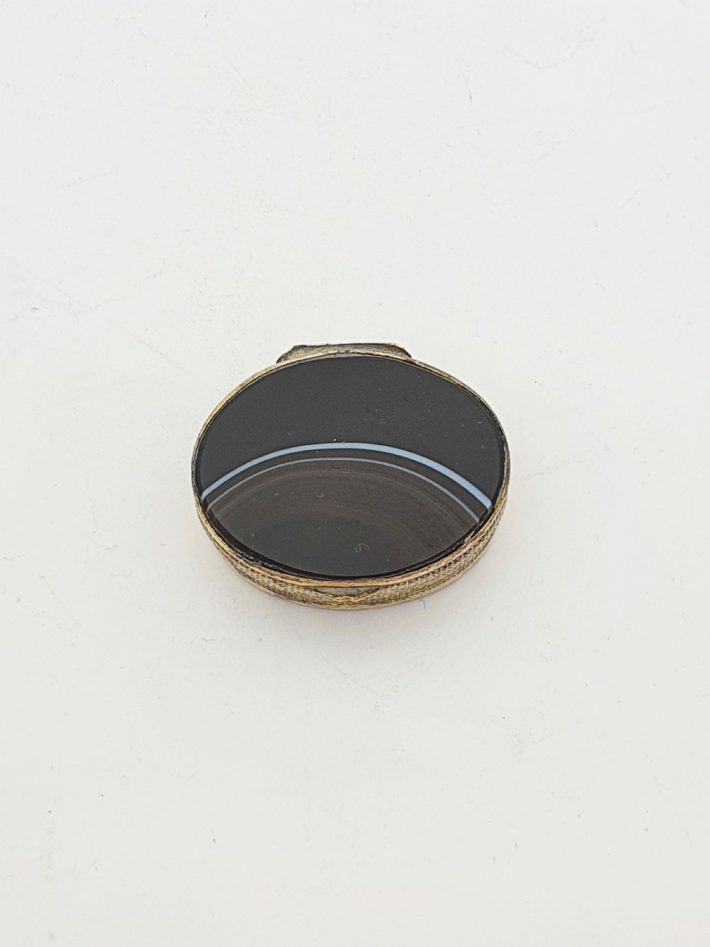 An open small oval Victorian gilt brass box with textured pattern engraving and polished banded agate panels set into the top and bottom. View III