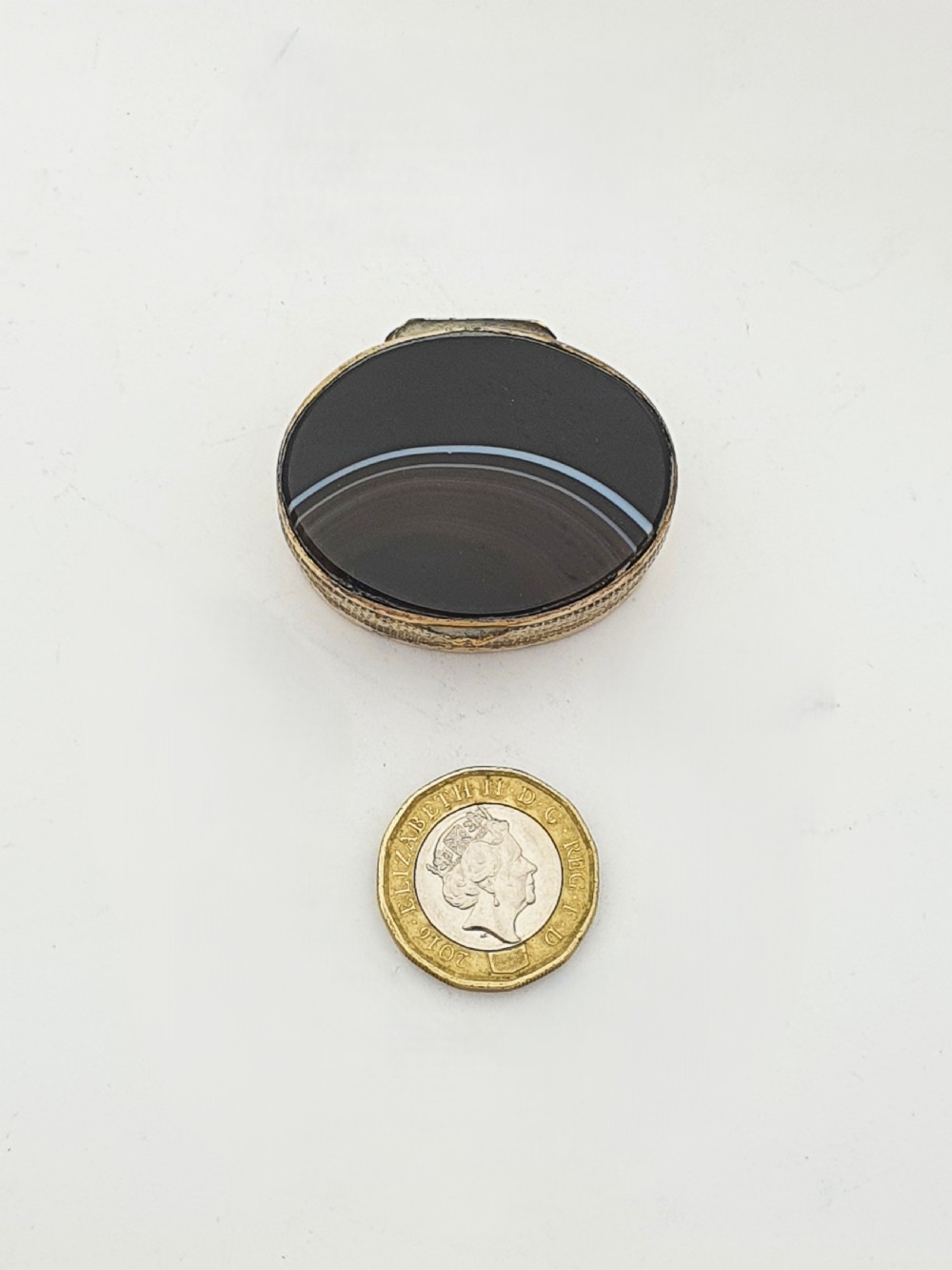 An open small oval Victorian gilt brass box with textured pattern engraving and polished banded agate panels set into the top and bottom. View IV