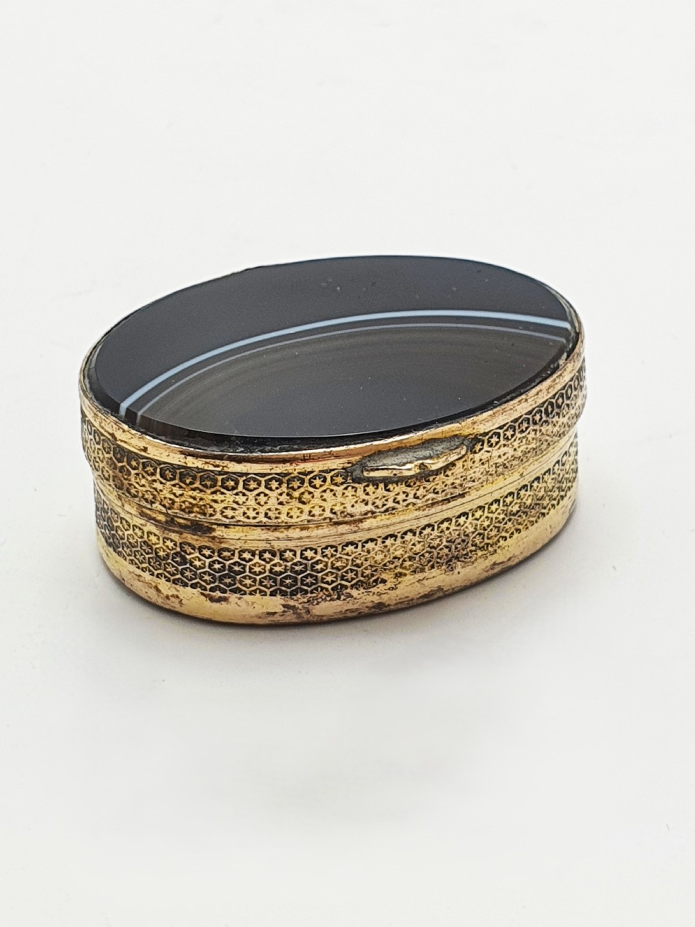 An open small oval Victorian gilt brass box with textured pattern engraving and polished banded agate panels set into the top and bottom. View V