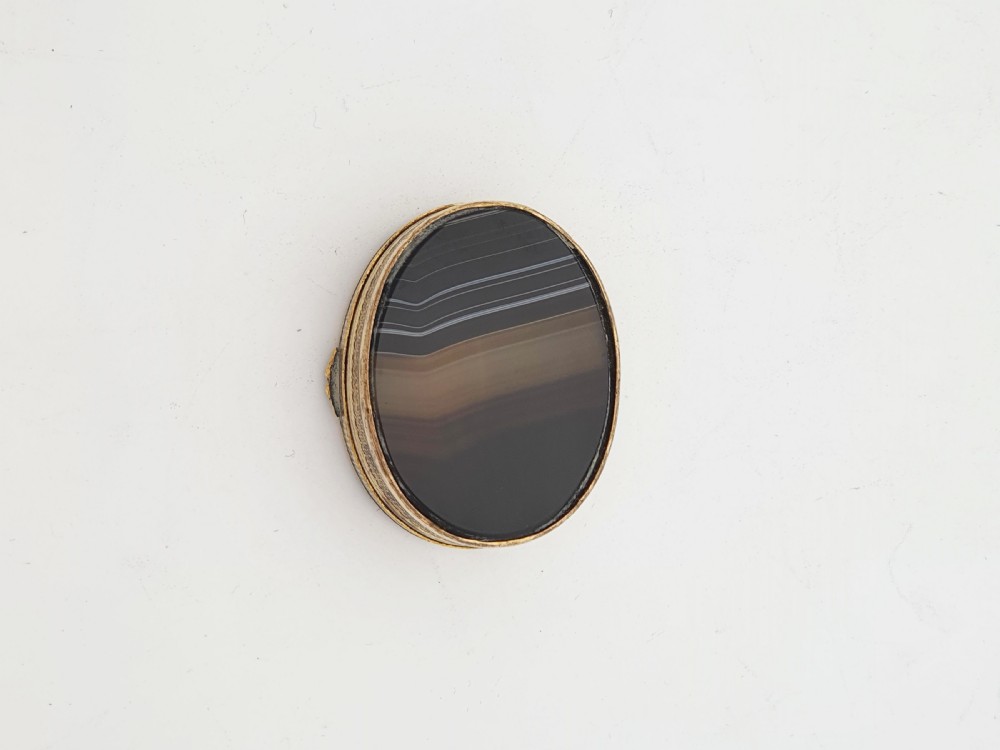 An open small oval Victorian gilt brass box with textured pattern engraving and polished banded agate panels set into the top and bottom. View VI