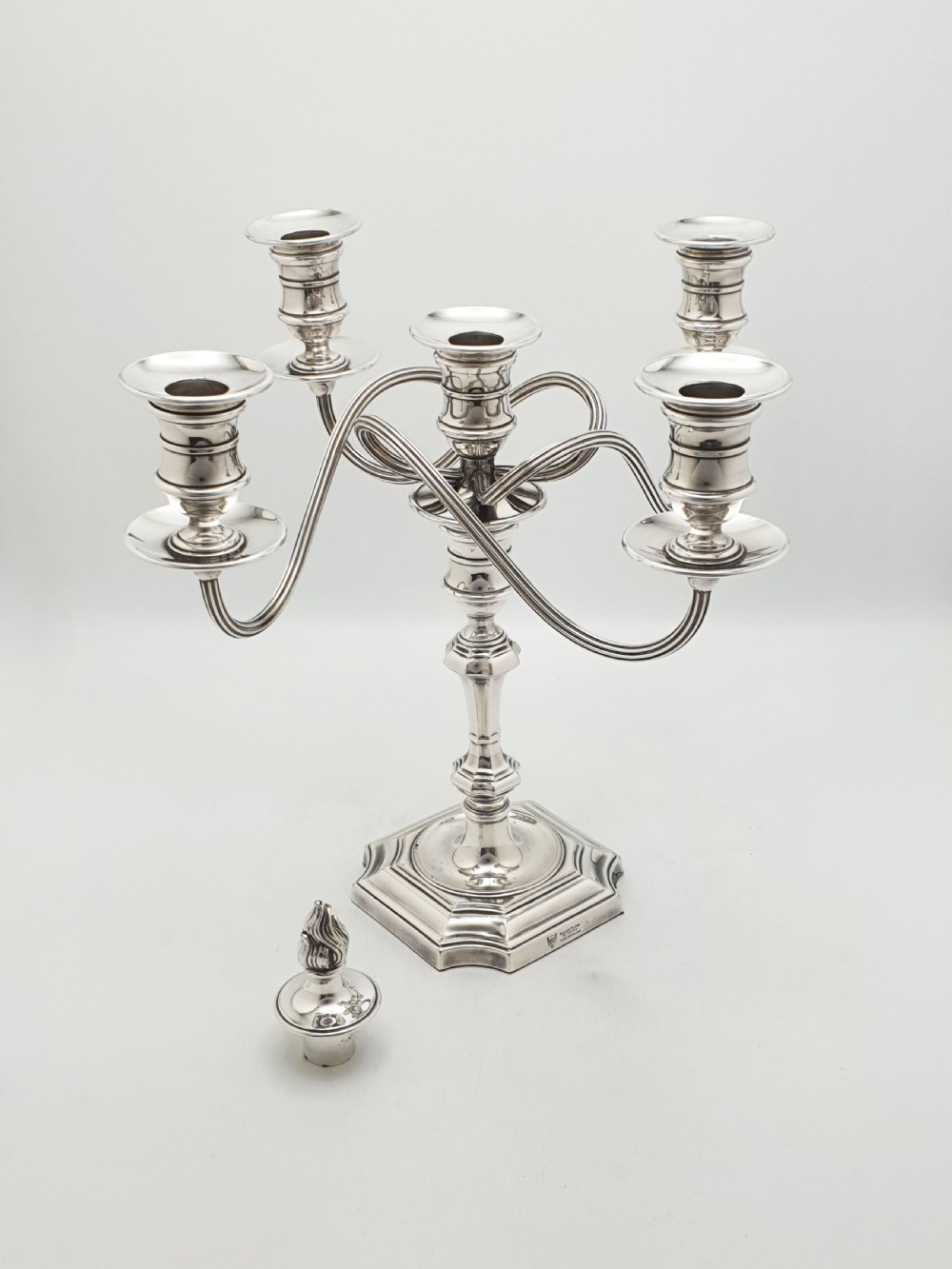 An Edwardian silver-plated five-light candelabrum featuring curved scrolling arms, urn-form sconces, a removable flame finial, and a stepped square base.