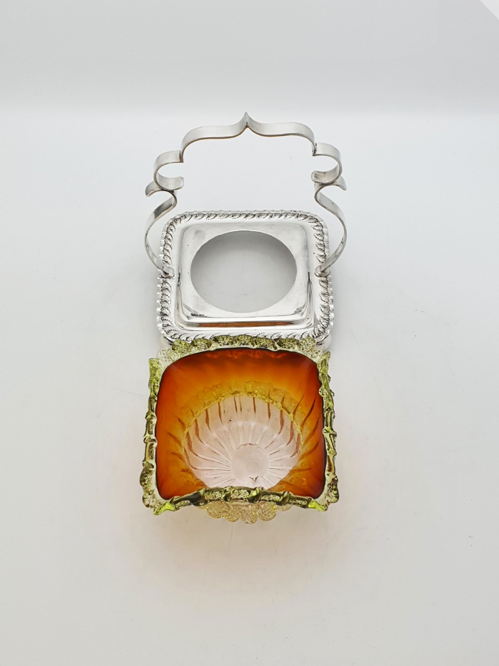 An Edwardian silver-plated stand with a shaped handle and ball feet holding a ruffled amber and yellow glass bonbon dish. View V