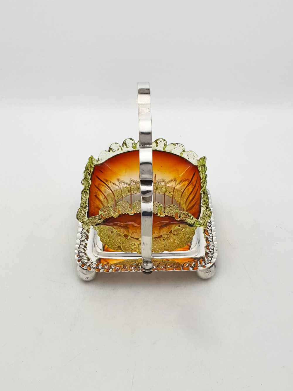 An Edwardian silver-plated stand with a shaped handle and ball feet holding a ruffled amber and yellow glass bonbon dish. View VI