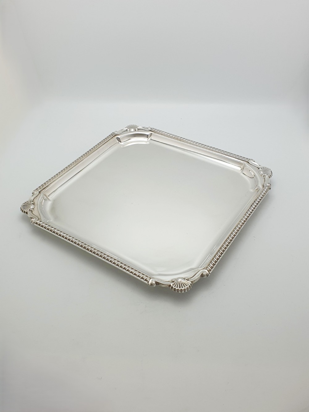 A square silver-plated cocktail tray featuring moulded shell motifs at the four corners and a gadrooned rim border.