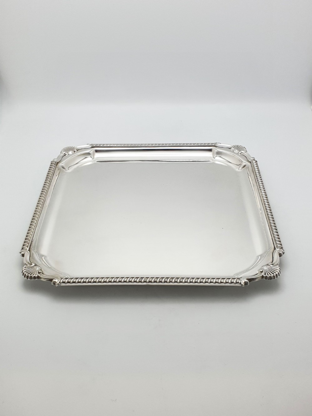 A square silver-plated cocktail tray featuring moulded shell motifs at the four corners and a gadrooned rim border. View III