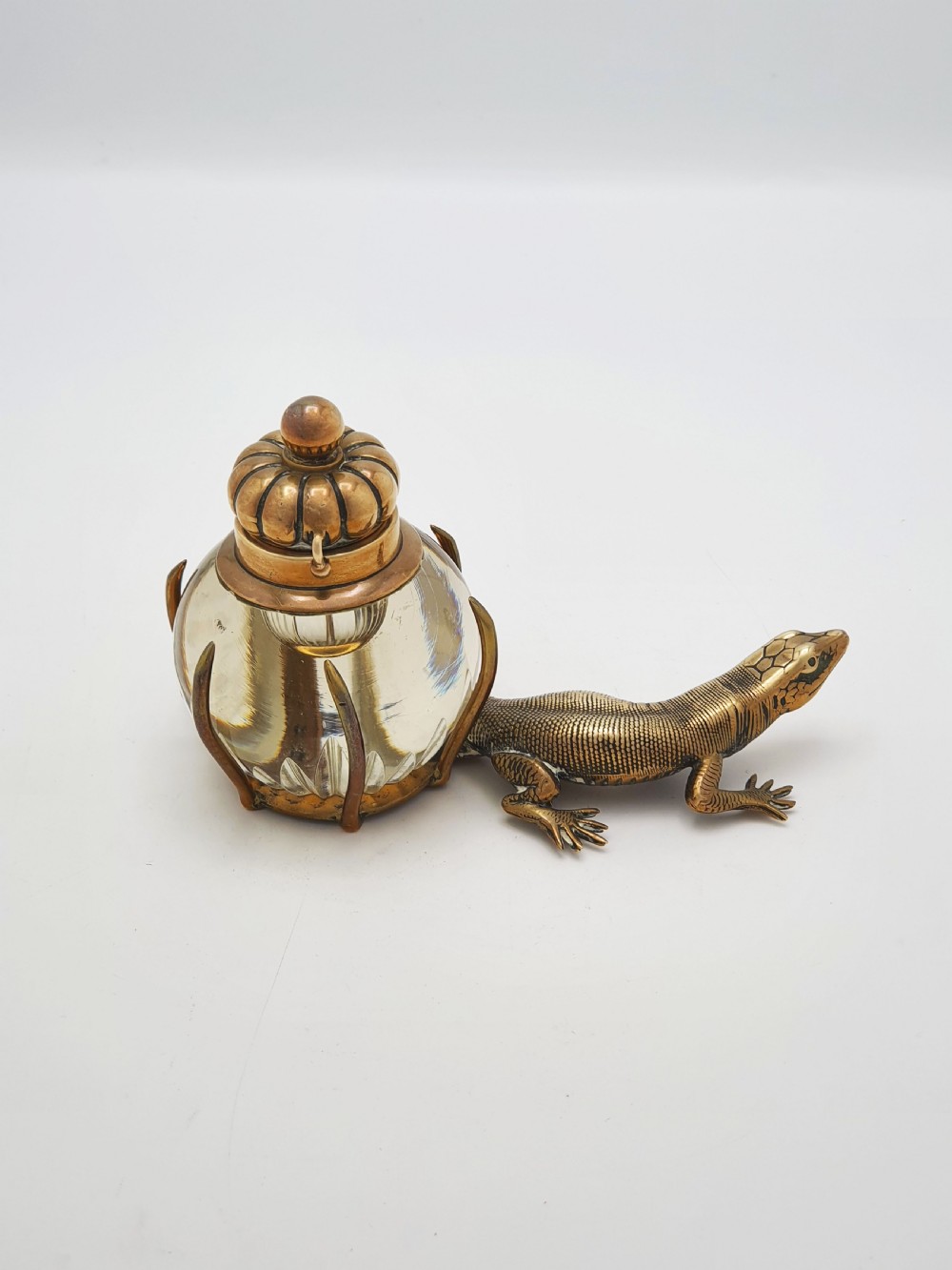 An antique Victorian brass inkstand featuring a cast lizard wrapped around a clear spherical glass inkwell with a crown-shaped hinged lid. View VI
