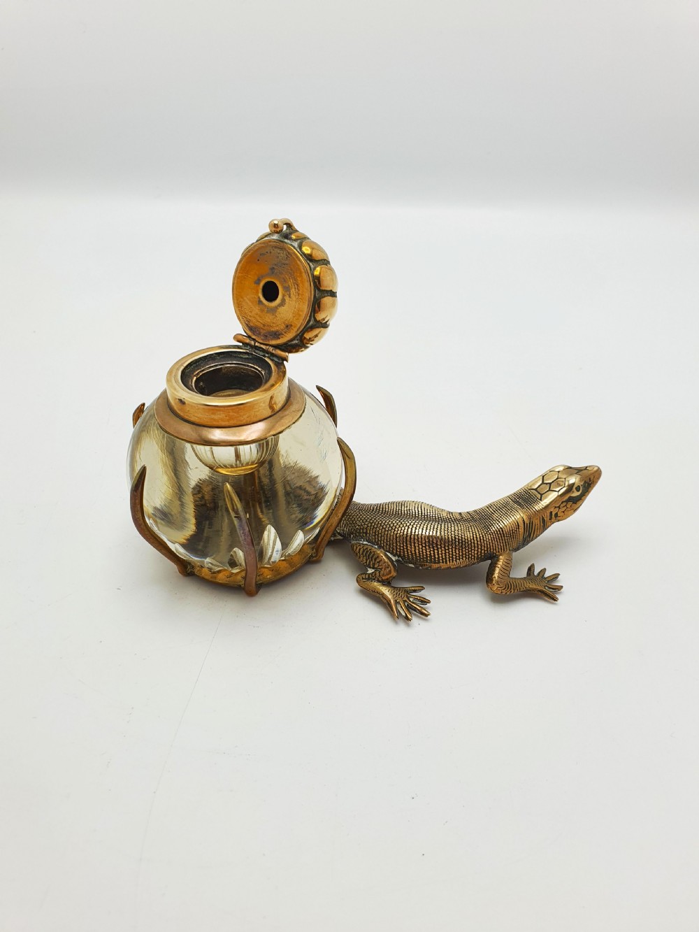 An antique Victorian brass inkstand featuring a cast lizard wrapped around a clear spherical glass inkwell with a crown-shaped hinged lid. View III