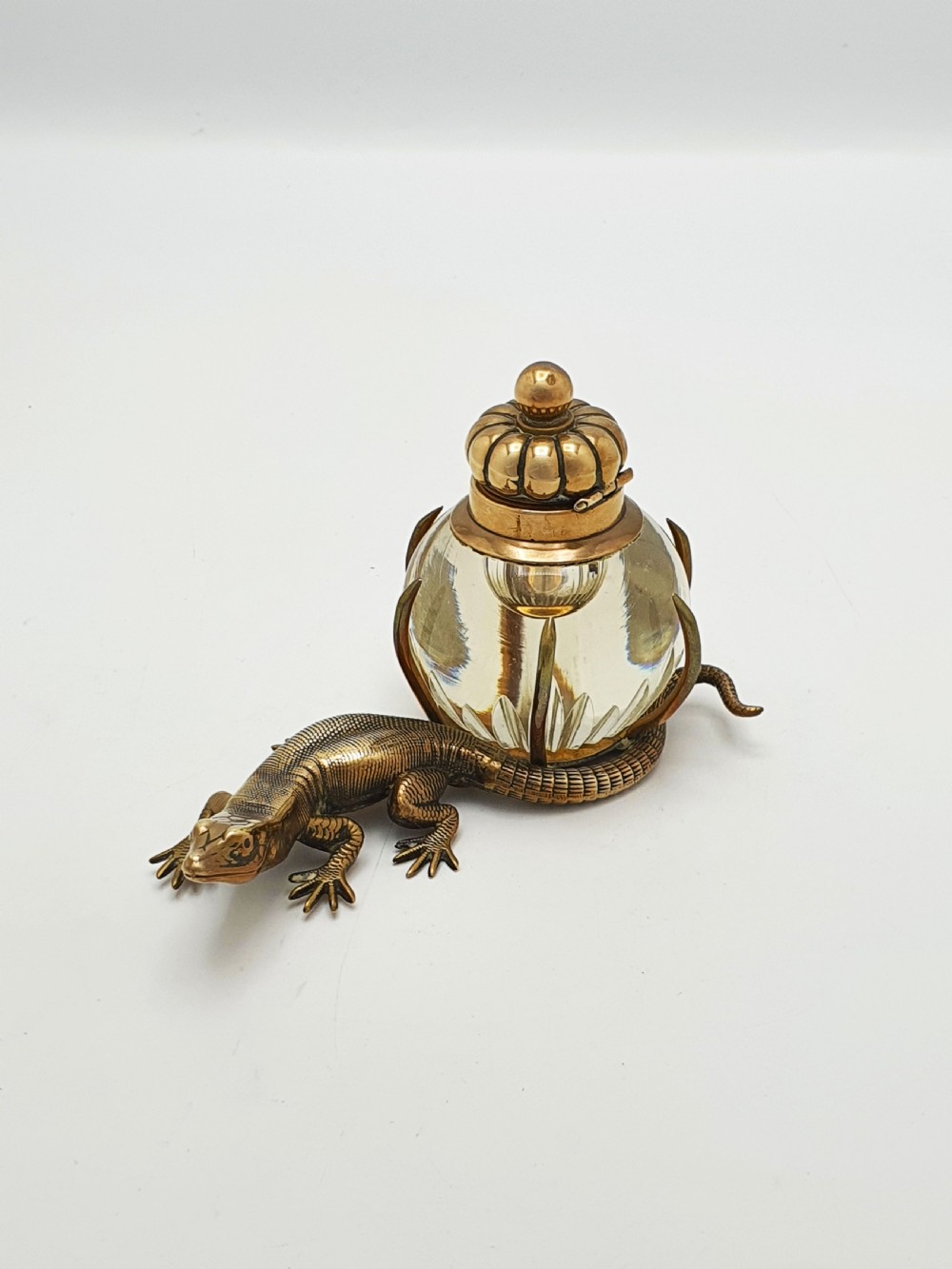 An antique Victorian brass inkstand featuring a cast lizard wrapped around a clear spherical glass inkwell with a crown-shaped hinged lid.