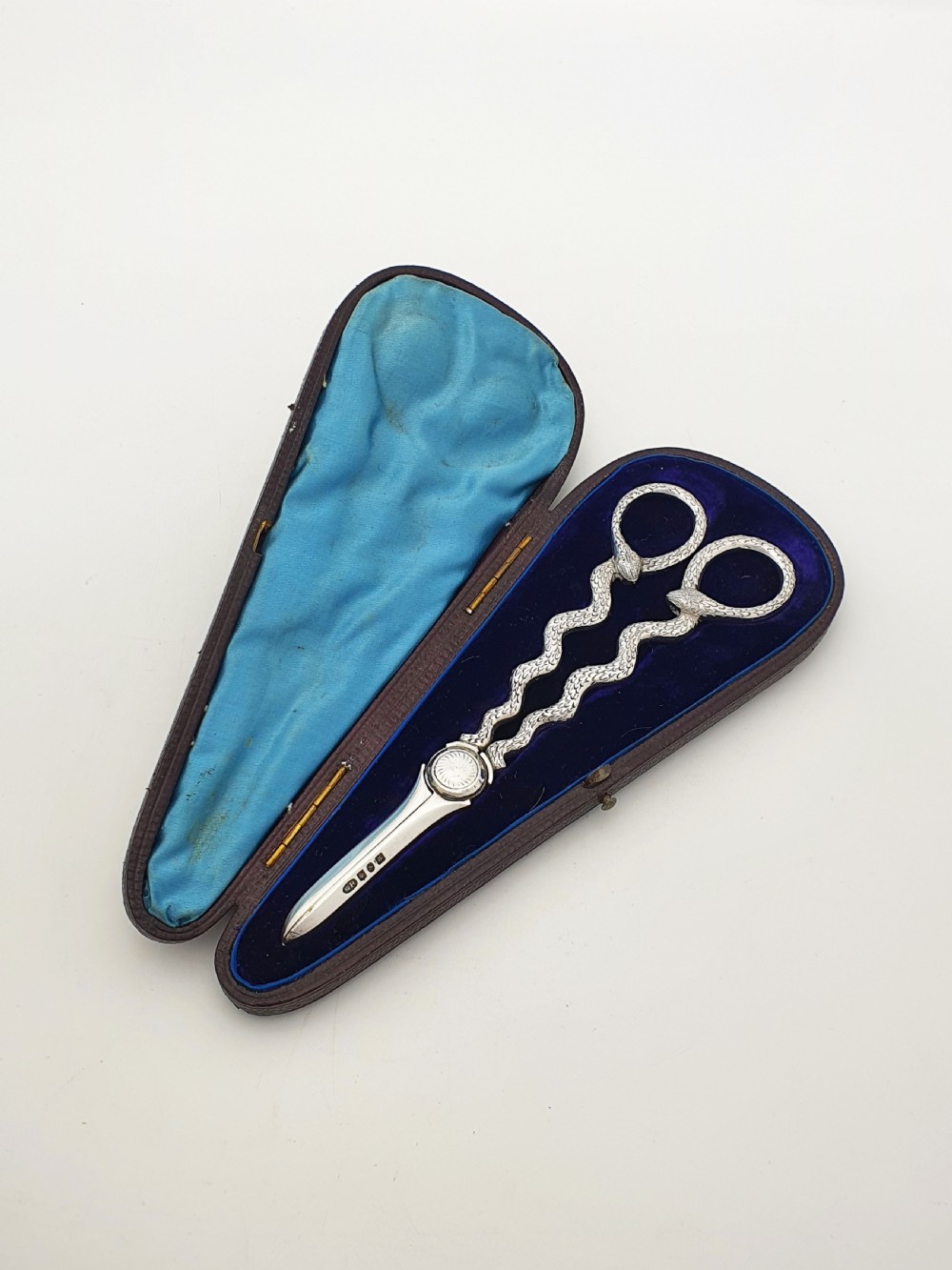 A pair of Victorian silver grape scissors with serpent-shaped handles, presented inside an open velvet-lined protective case.
