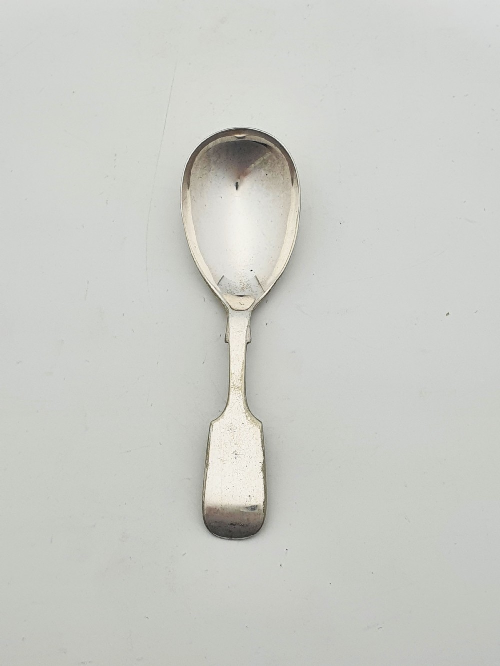 An oval silver tea caddy featuring lion mask ring handles on the sides, a hinged lid with beaded edging, and a front clip holding a small silver caddy spoon. View IX
