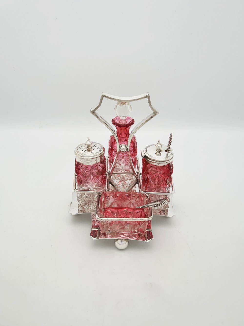 An Edwardian silver-plated stand holding four diamond-cut cranberry flashed glass condiment bottles and jars.