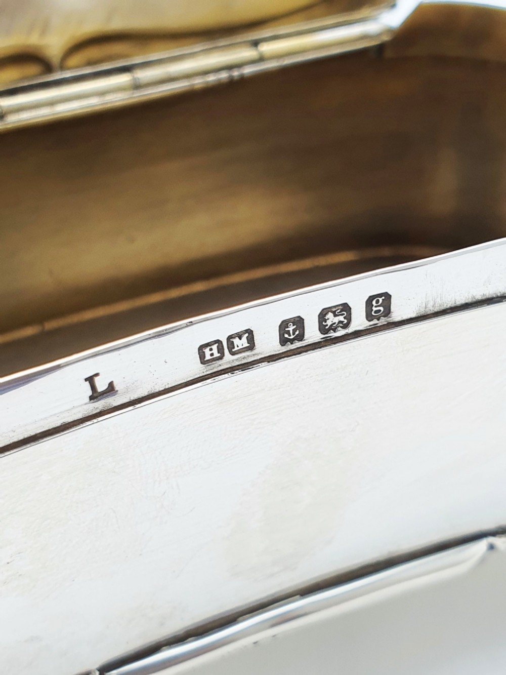 An Edwardian sterling silver trinket box featuring an embossed lid depicting cherub heads and a scrolling border, supported by four cast feet. View V