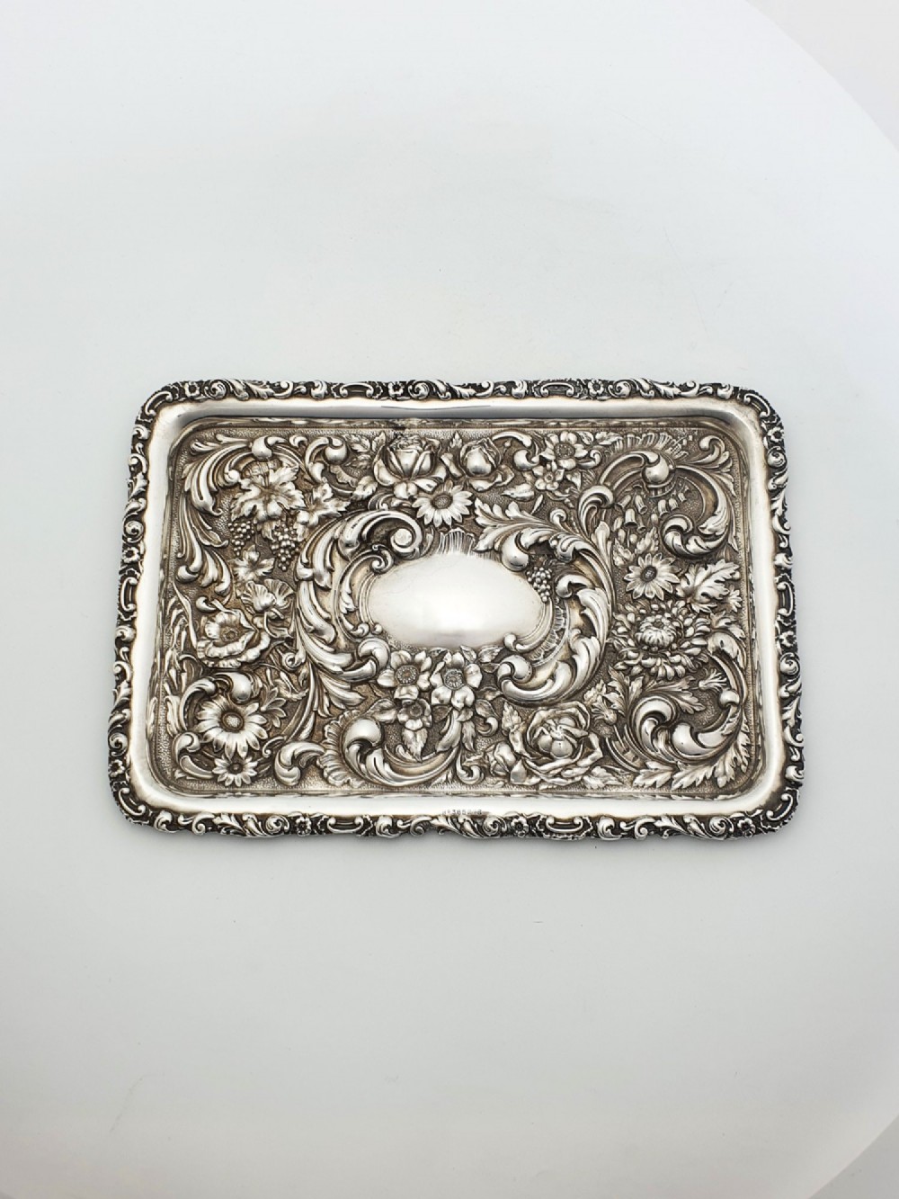 A rectangular sterling silver tray decorated with raised floral repousse patterns and an unengraved central cartouche.