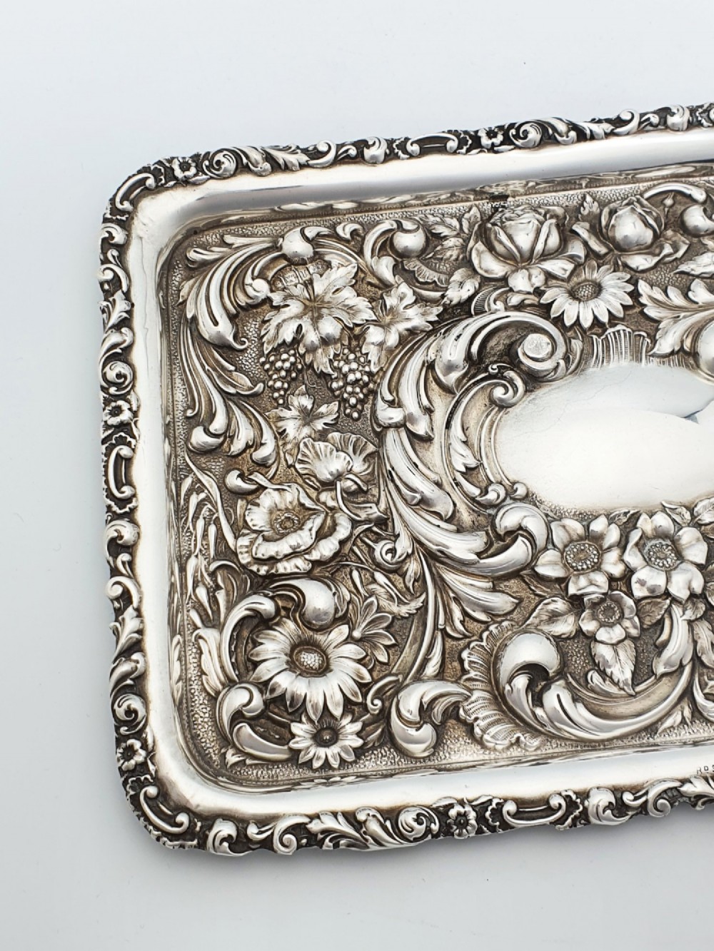 A rectangular sterling silver tray decorated with raised floral repousse patterns and an unengraved central cartouche. View III