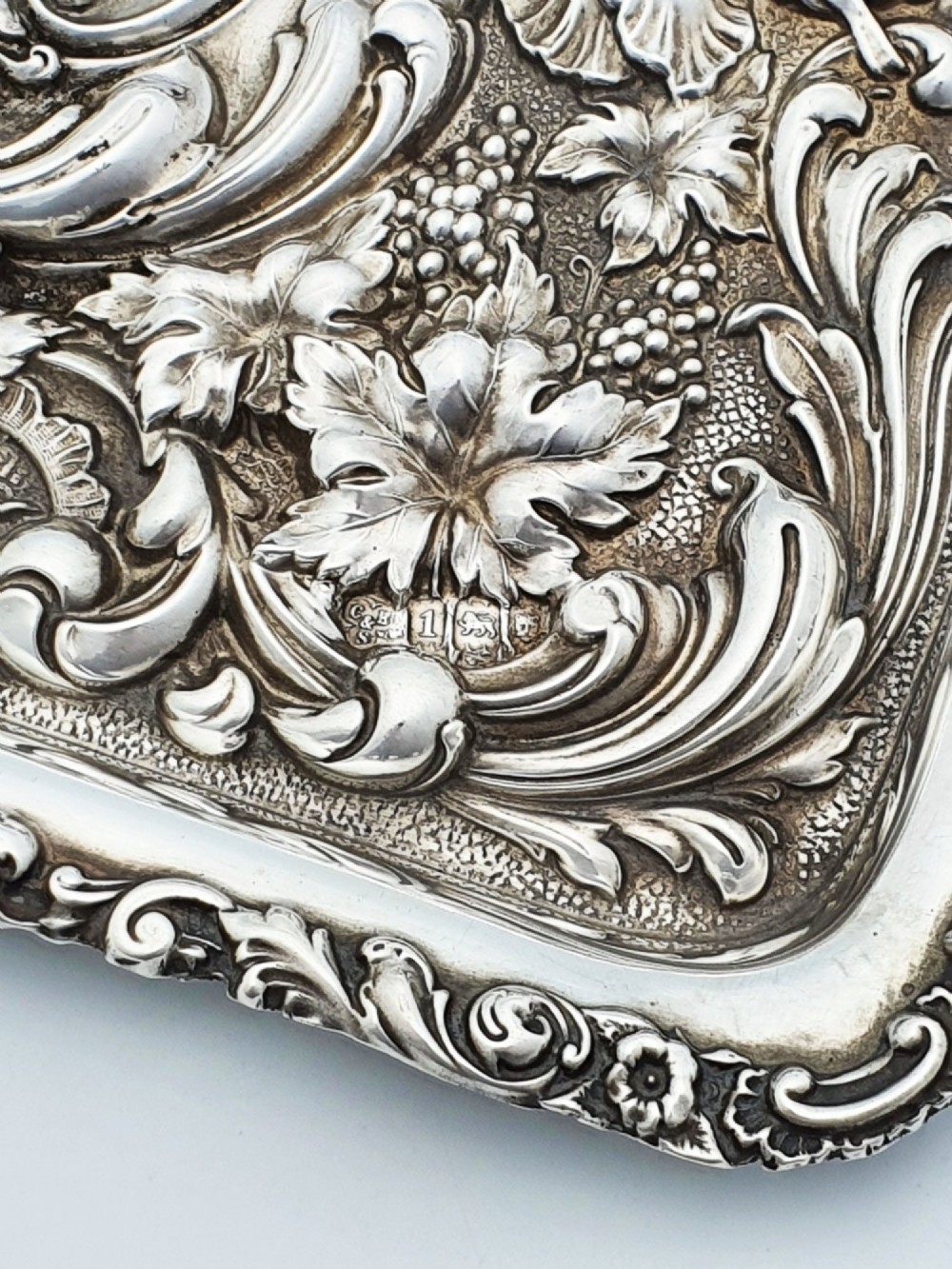 A rectangular sterling silver tray decorated with raised floral repousse patterns and an unengraved central cartouche. View V