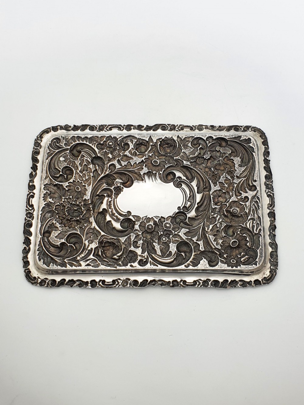 A rectangular sterling silver tray decorated with raised floral repousse patterns and an unengraved central cartouche. View VI