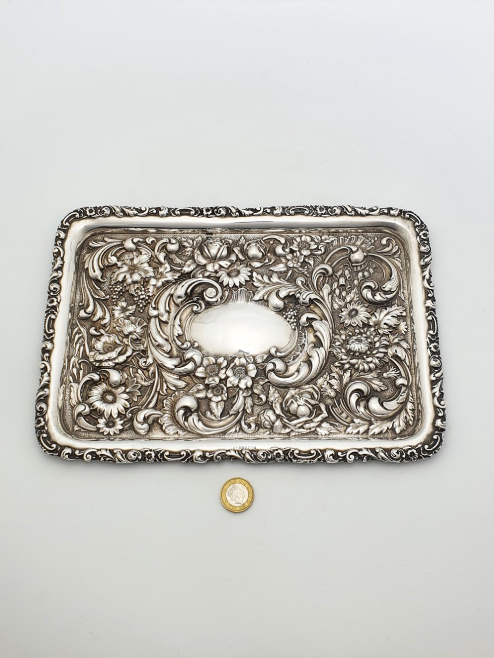 A rectangular sterling silver tray decorated with raised floral repousse patterns and an unengraved central cartouche. View VII