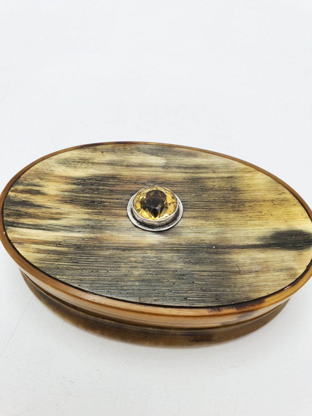 An oval Victorian snuff box made from natural mottled horn featuring a central faceted yellow citrine gem mounted on the lid.