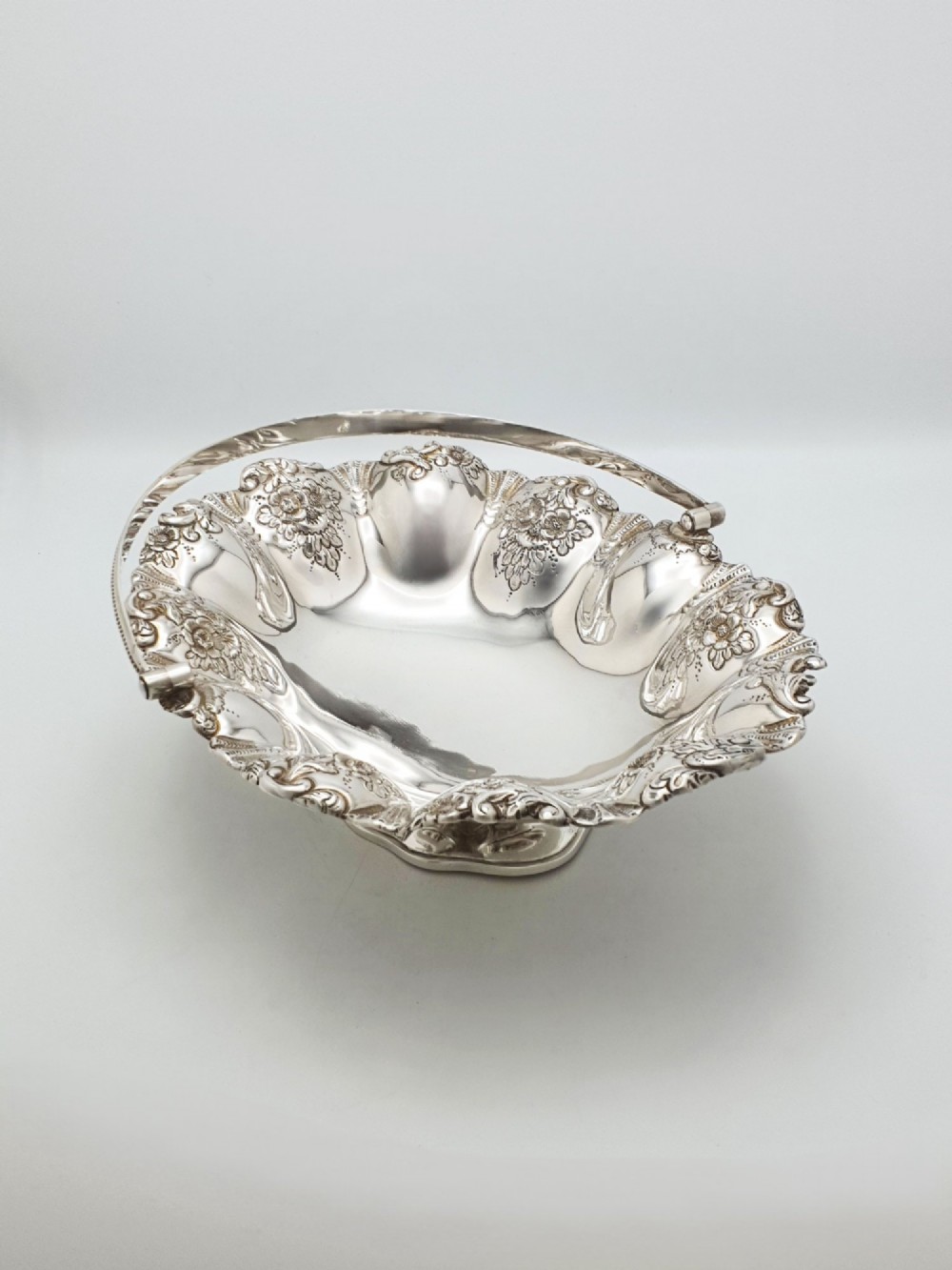 An Edwardian silver-plated oval basket featuring an overhead swing handle, fluted lobes, and a floral repousse rim. View III