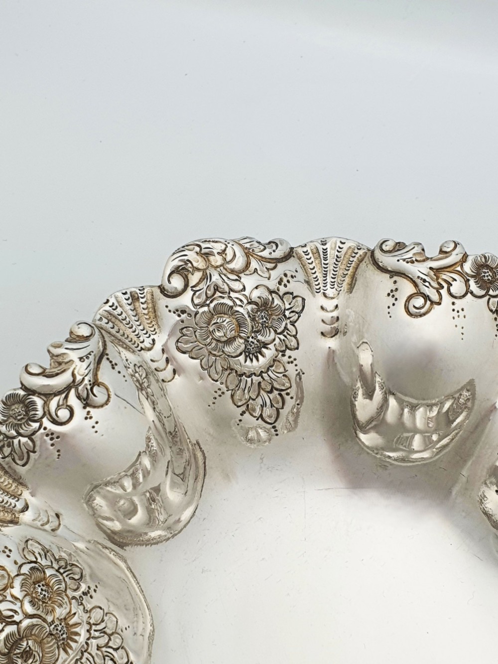 An Edwardian silver-plated oval basket featuring an overhead swing handle, fluted lobes, and a floral repousse rim. View IV
