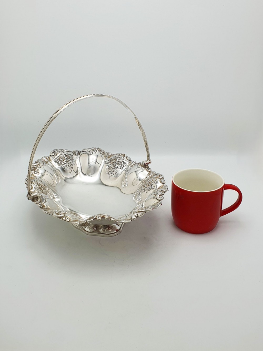 An Edwardian silver-plated oval basket featuring an overhead swing handle, fluted lobes, and a floral repousse rim. View VII