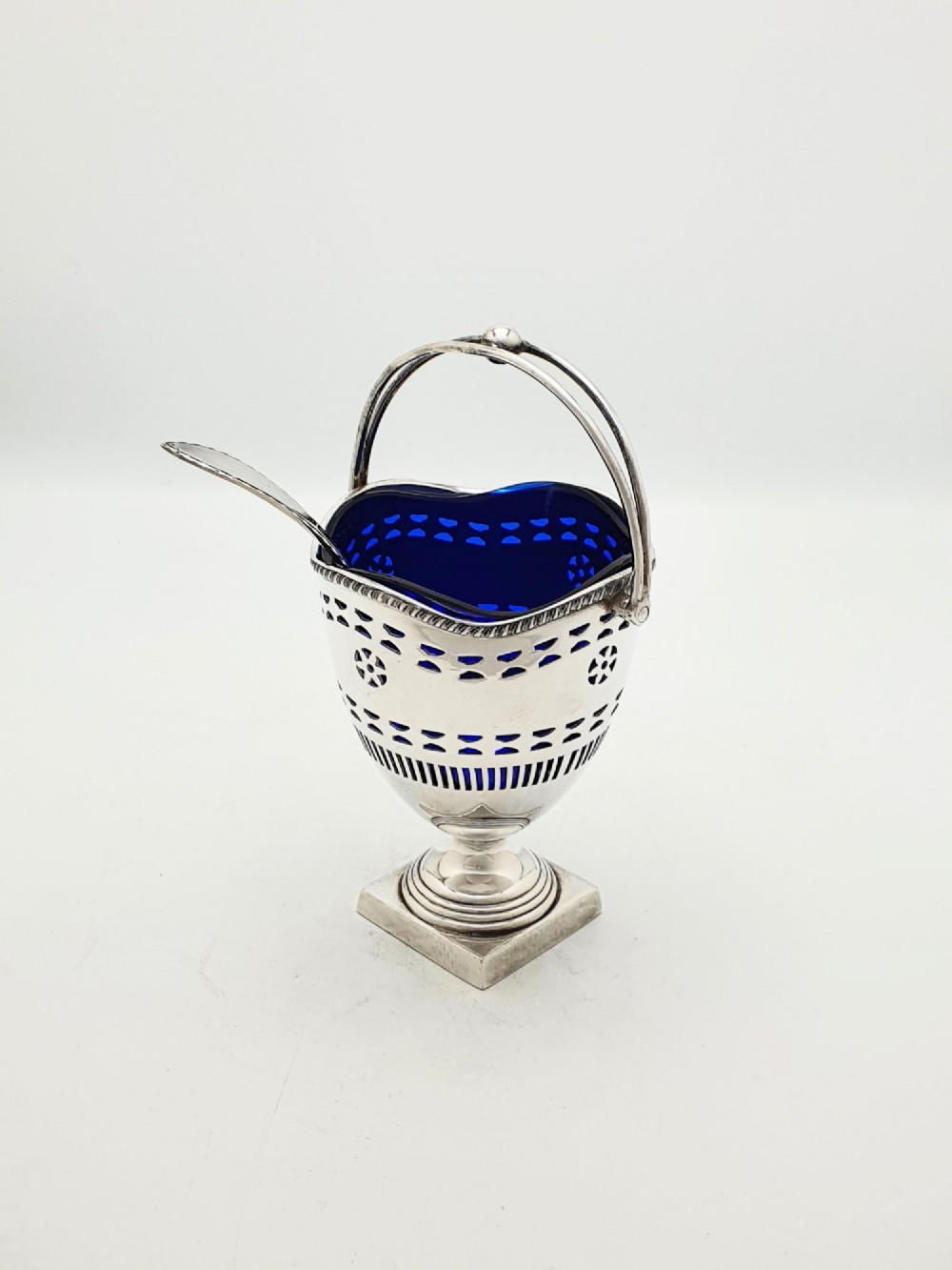 A silver-plated pierced pedestal sugar basket with a swing handle, cobalt blue glass liner, and accompanying sifter spoon. View II