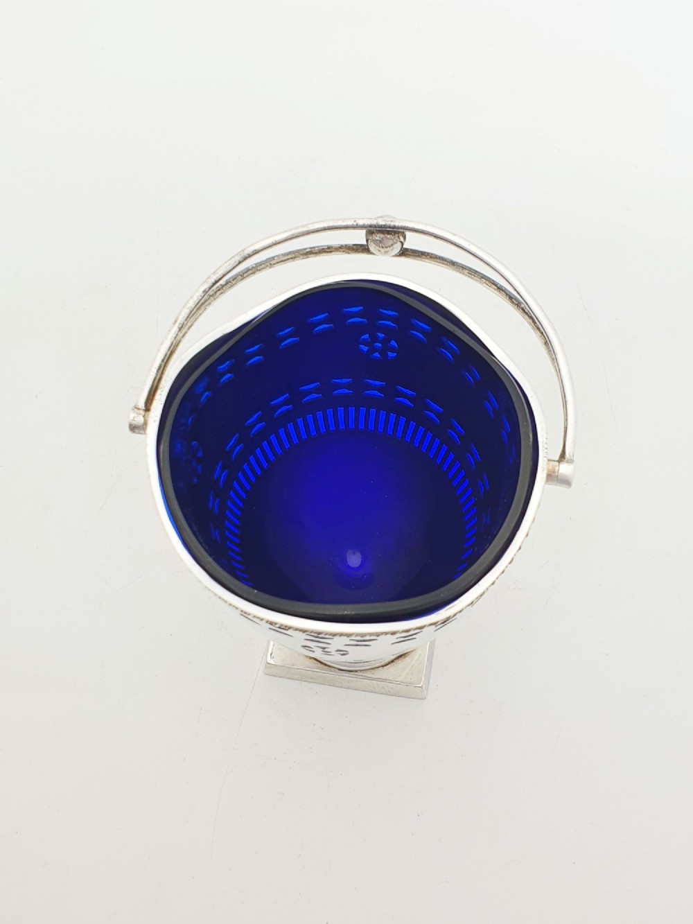 A silver-plated pierced pedestal sugar basket with a swing handle, cobalt blue glass liner, and accompanying sifter spoon. View III