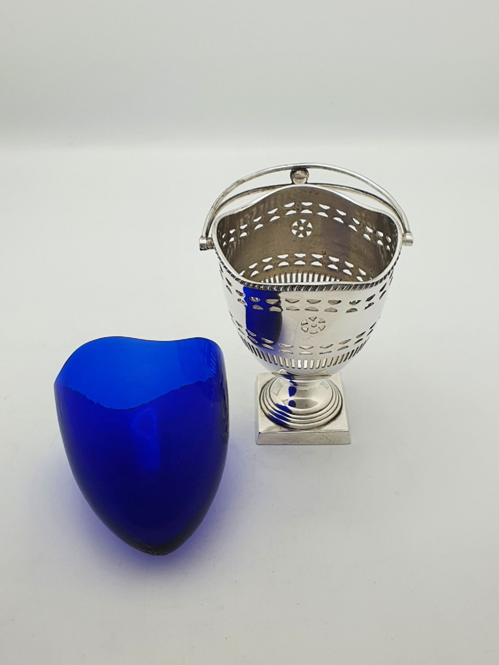 A silver-plated pierced pedestal sugar basket with a swing handle, cobalt blue glass liner, and accompanying sifter spoon. View IV