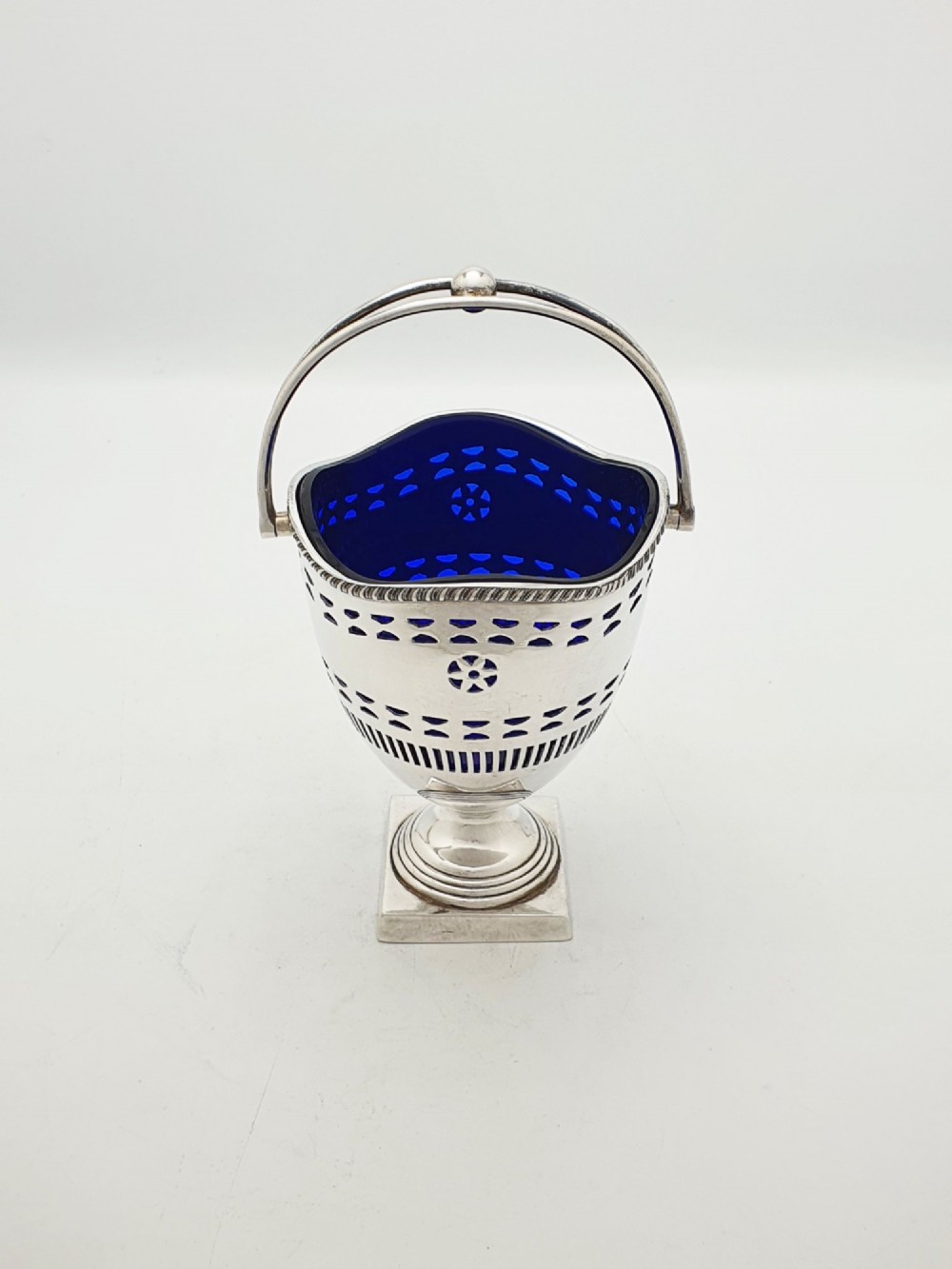 A silver-plated pierced pedestal sugar basket with a swing handle, cobalt blue glass liner, and accompanying sifter spoon. View VII
