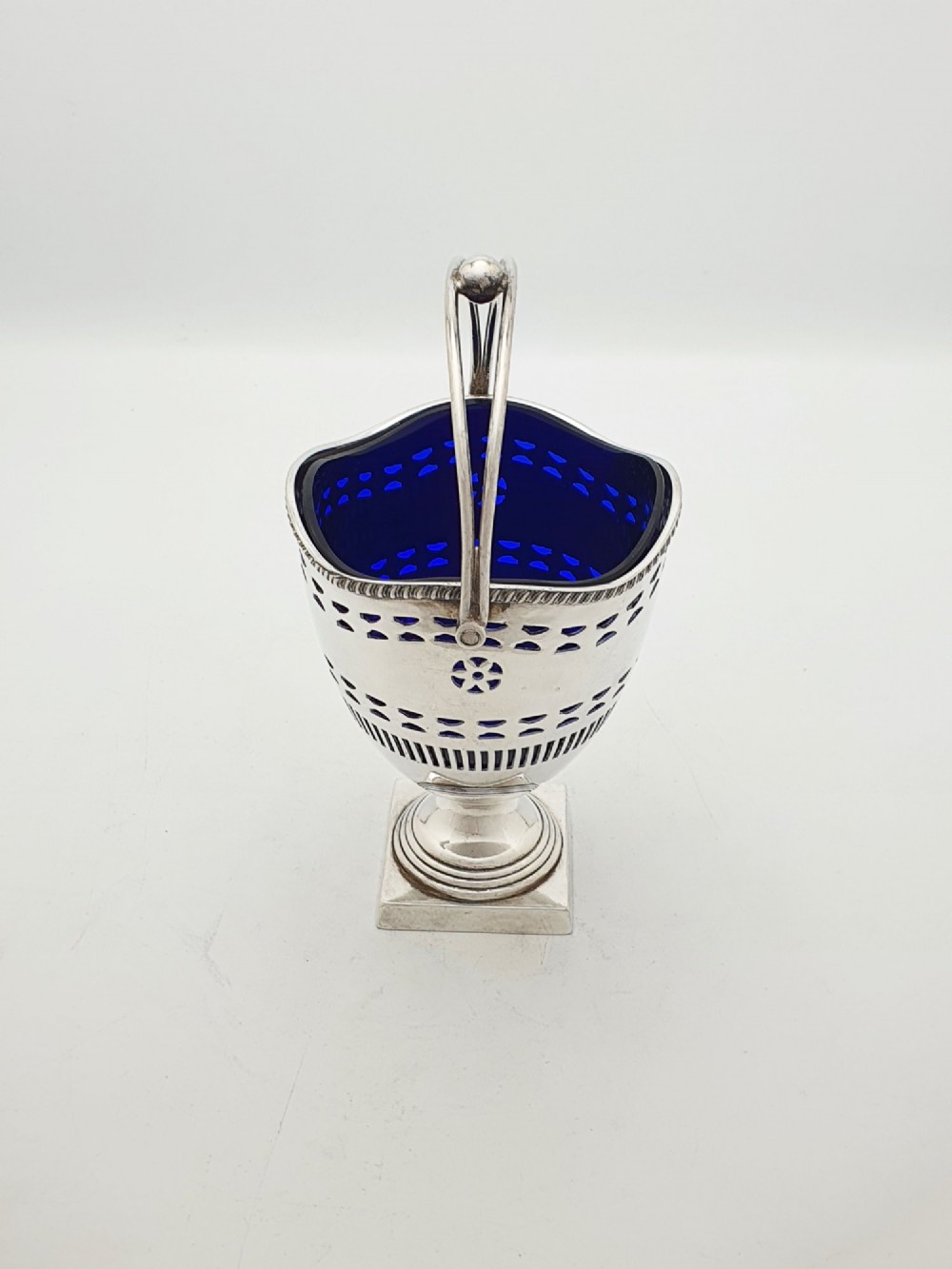 A silver-plated pierced pedestal sugar basket with a swing handle, cobalt blue glass liner, and accompanying sifter spoon. View VIII