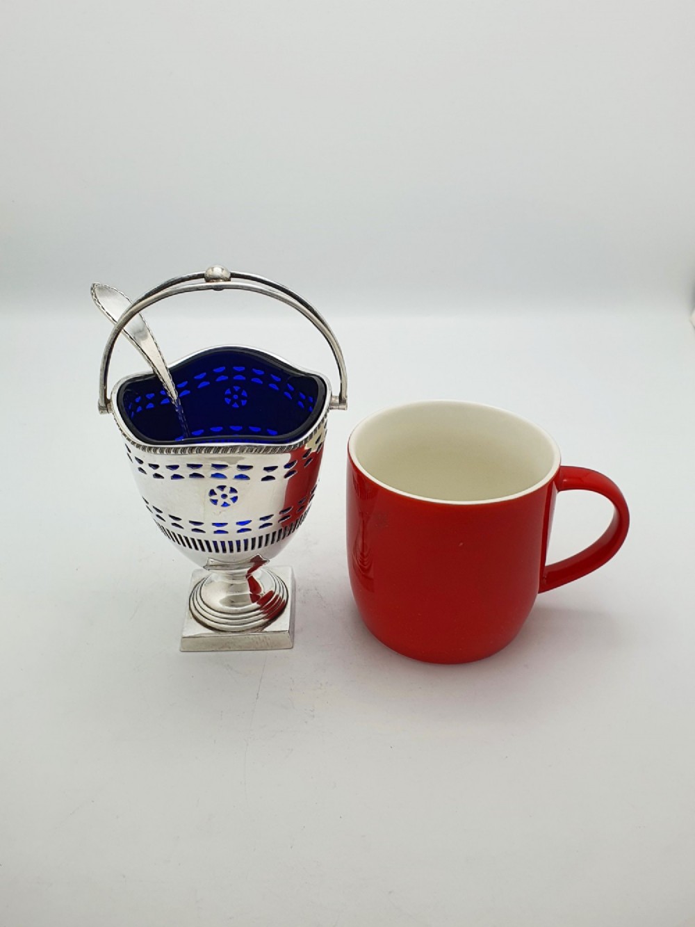 A silver-plated pierced pedestal sugar basket with a swing handle, cobalt blue glass liner, and accompanying sifter spoon. View X