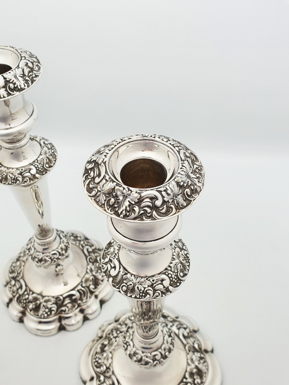 A pair of polished silver-plated candlesticks featuring ornate foliate repousse borders on scalloped bases. View II