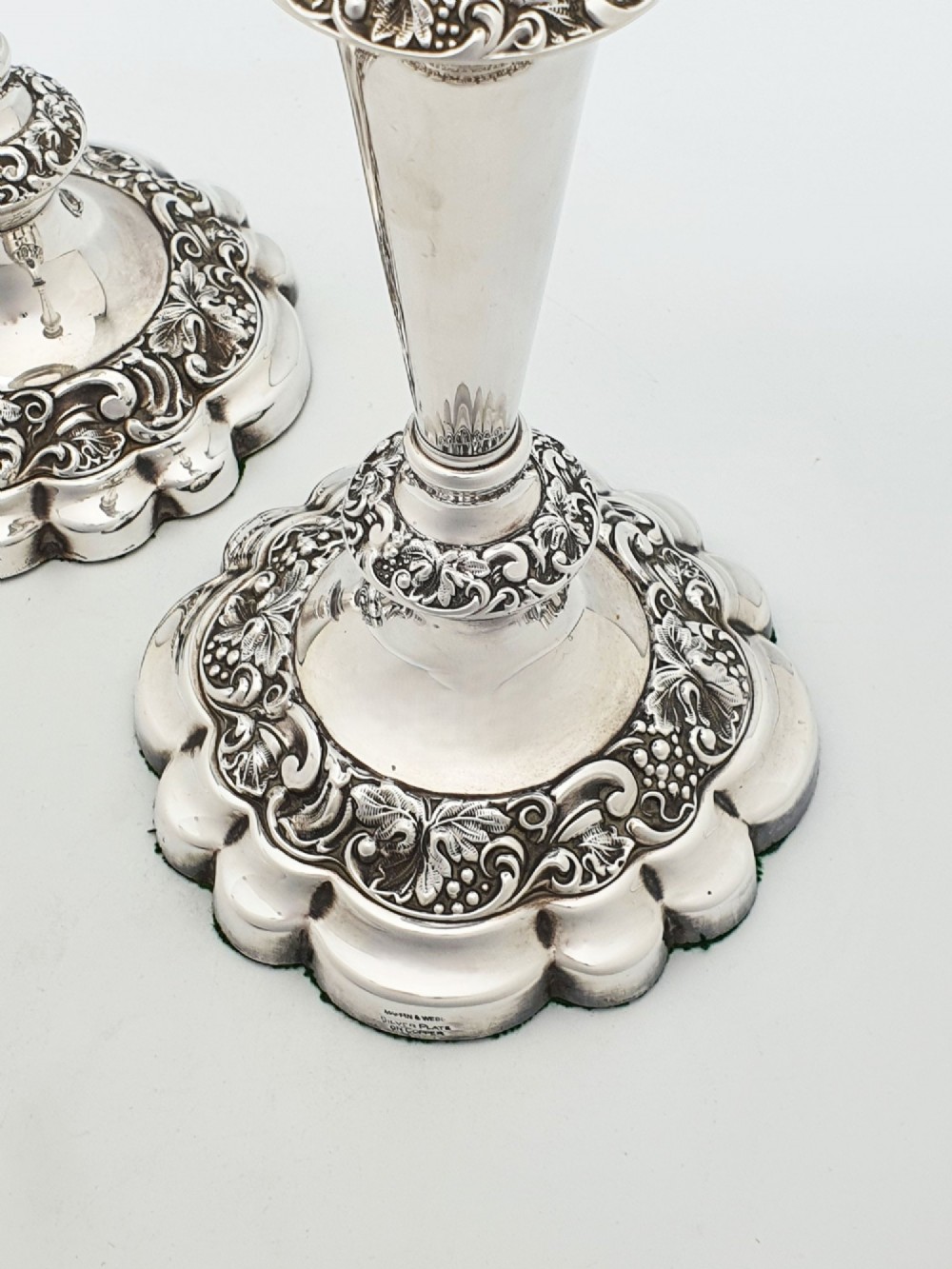 A pair of polished silver-plated candlesticks featuring ornate foliate repousse borders on scalloped bases. View III