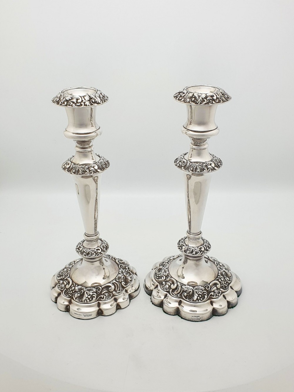 A pair of polished silver-plated candlesticks featuring ornate foliate repousse borders on scalloped bases. View IV
