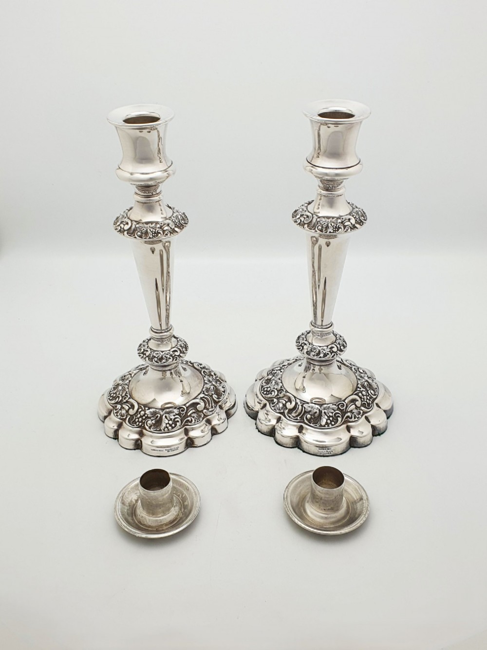 A pair of polished silver-plated candlesticks featuring ornate foliate repousse borders on scalloped bases. View VII