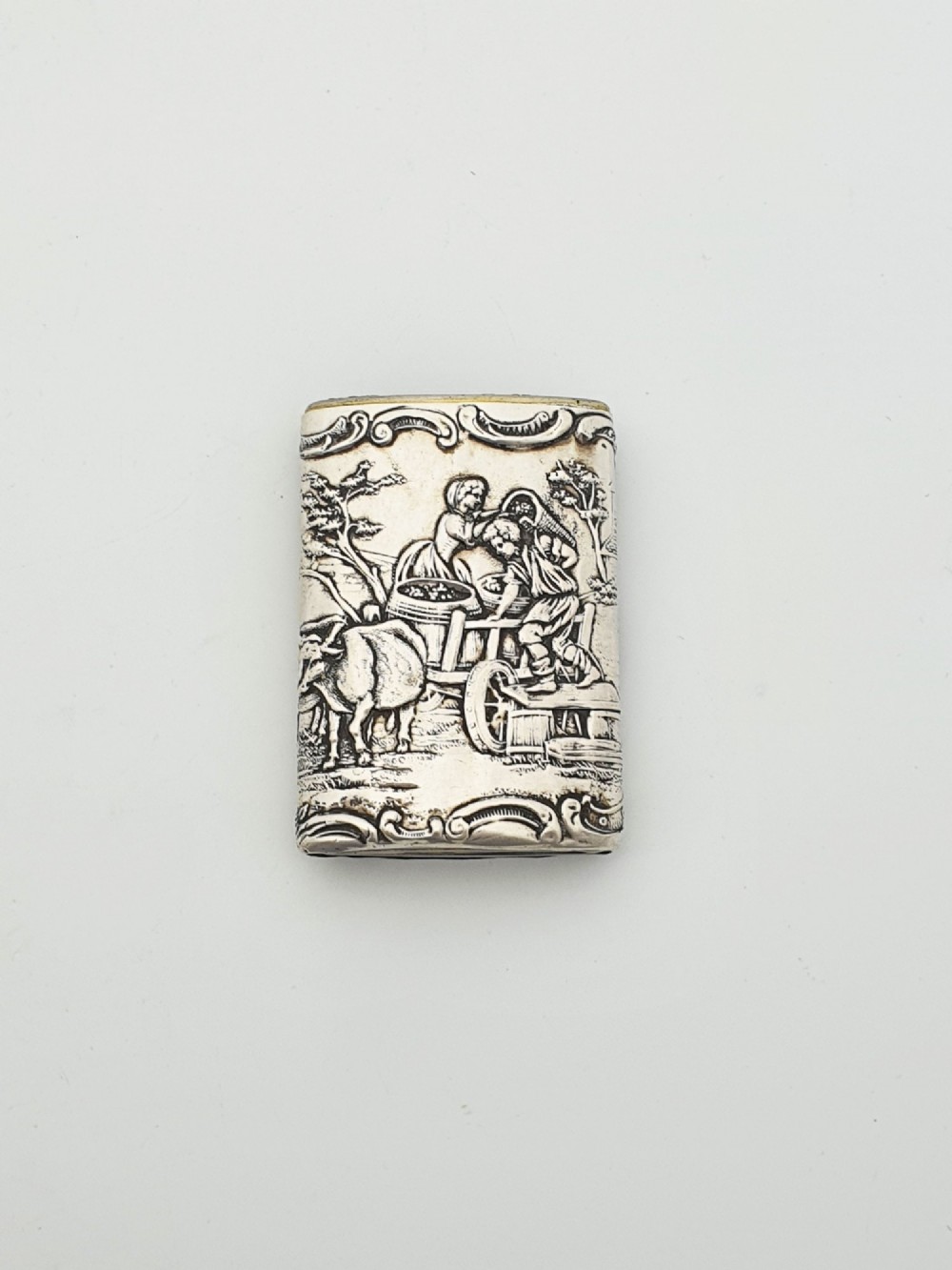 A rectangular silver vesta case with detailed embossed scrollwork around a scenic relief of a figure by water, featuring a sliding gilt interior compartment. View III