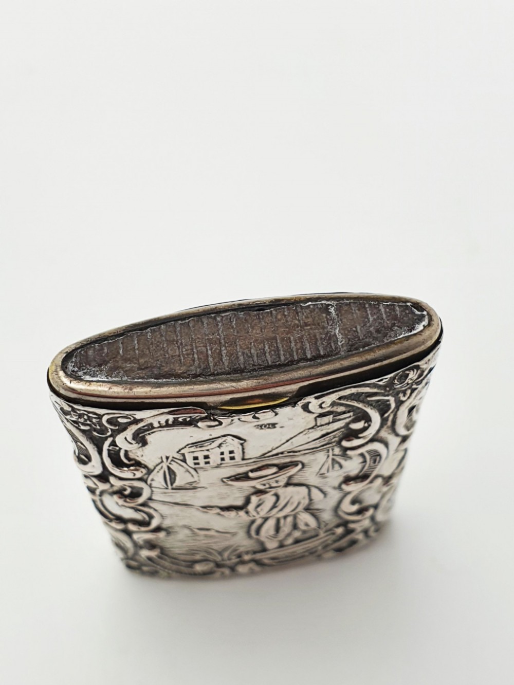 A rectangular silver vesta case with detailed embossed scrollwork around a scenic relief of a figure by water, featuring a sliding gilt interior compartment. View V