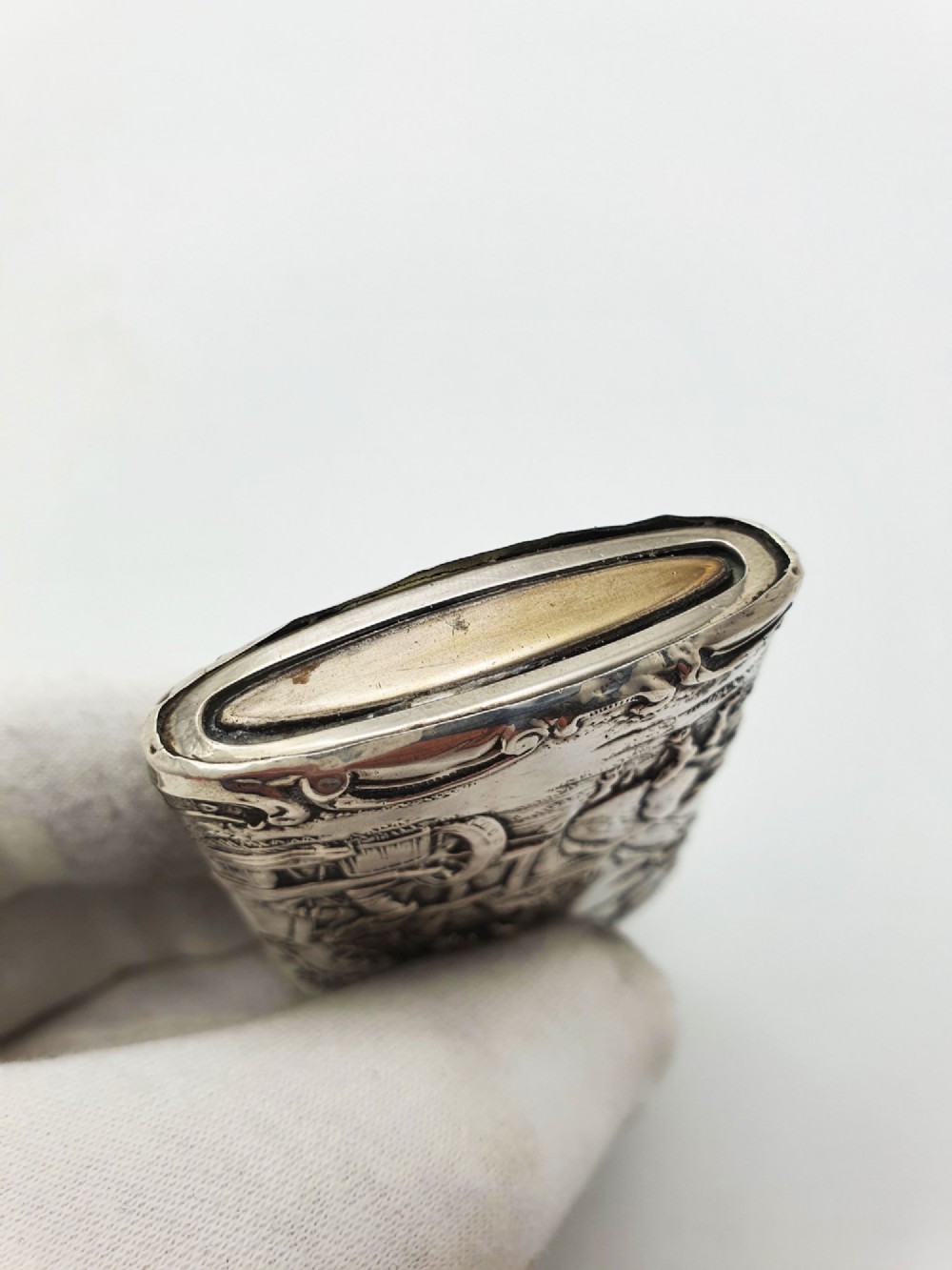 A rectangular silver vesta case with detailed embossed scrollwork around a scenic relief of a figure by water, featuring a sliding gilt interior compartment. View VI