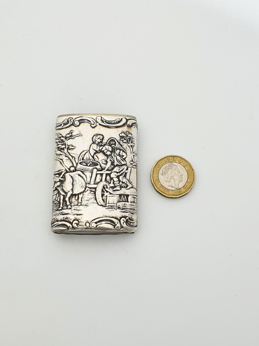 A rectangular silver vesta case with detailed embossed scrollwork around a scenic relief of a figure by water, featuring a sliding gilt interior compartment. View VII