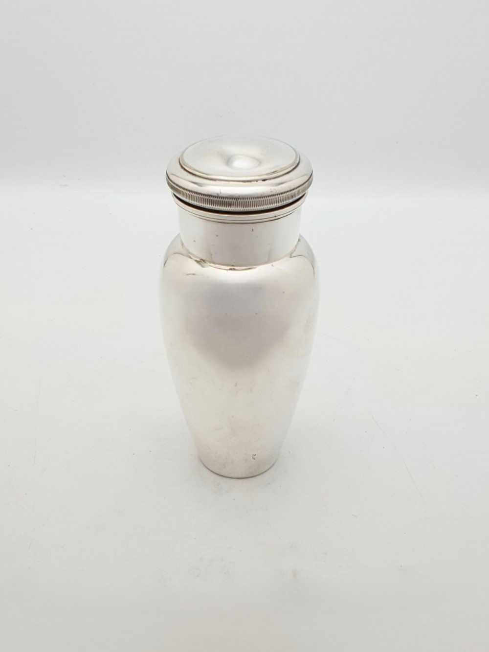 A silver-plated Art Deco bachelor cocktail shaker featuring a baluster body, milled collar, and a domed cap. View VI