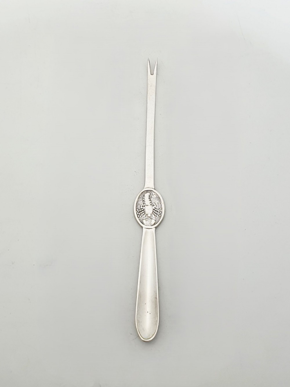 A set of twelve silver-plated lobster picks featuring embossed lobster medallions on the handles and narrow two-pronged tips, arranged neatly in a diagonal row. View VI