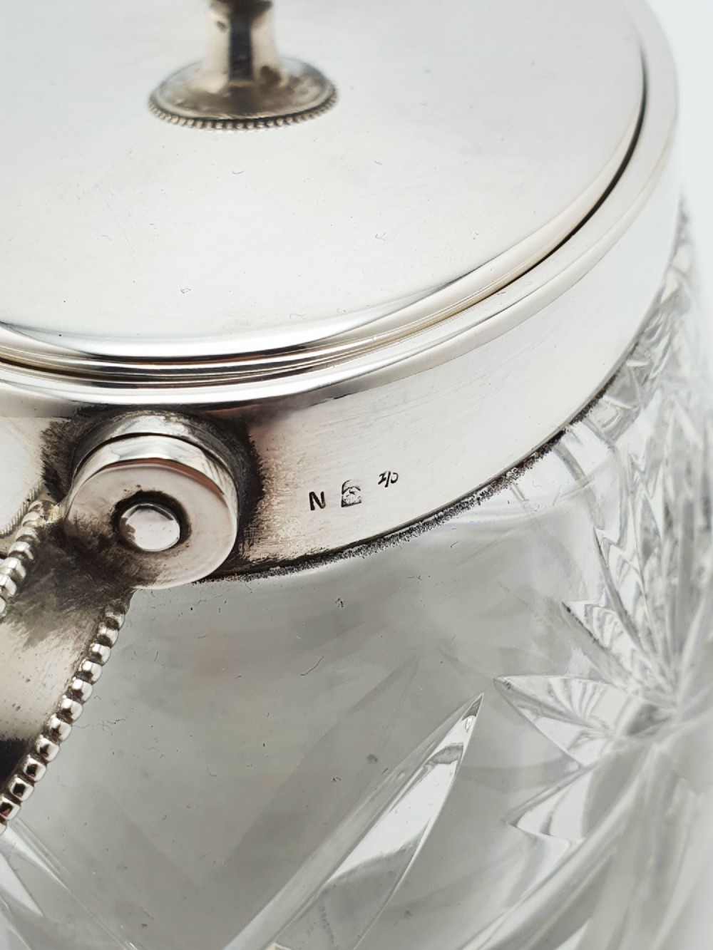 An oval cut glass biscuit box featuring a starburst motif, fitted with a silver-plated lid, central finial, and a beaded swing handle. View VIII